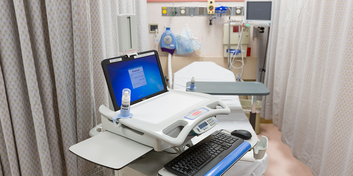 An image of a small container of Symmetry Hand Sanitizer attached to a mobile computer unit inside a hospital
