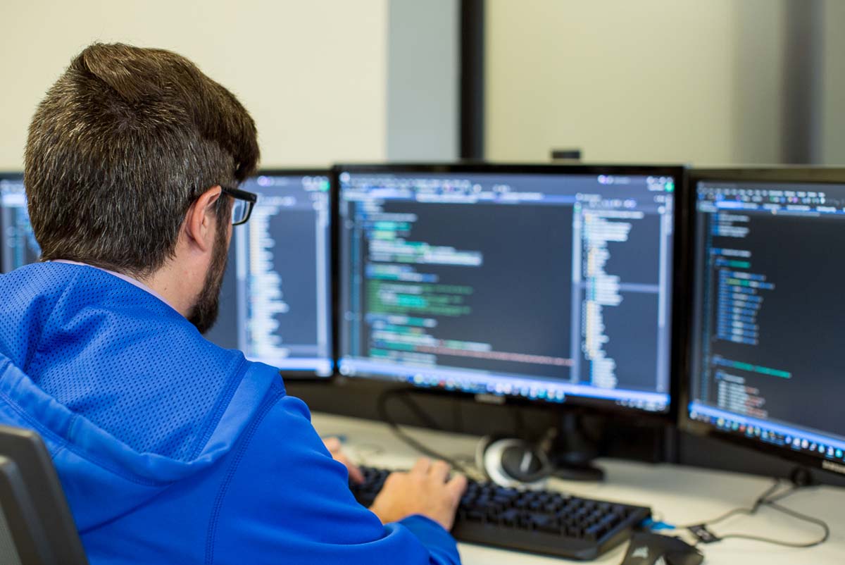 An image of Jason, of the Loft, working on web development with three screens full of code